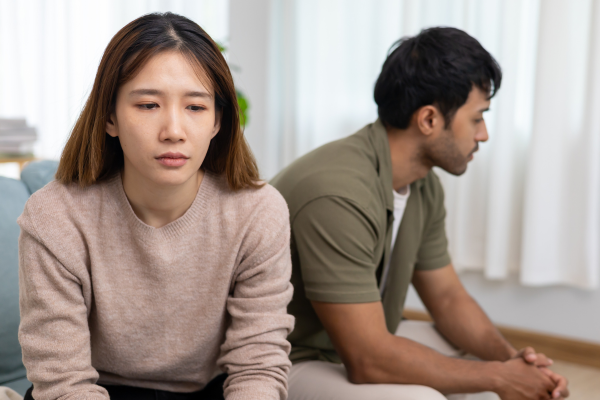 Man and woman sitting on couch with upset expressions on their faces.