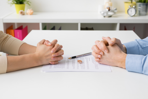 Man and woman holding their own hands over table with divorce papers.
